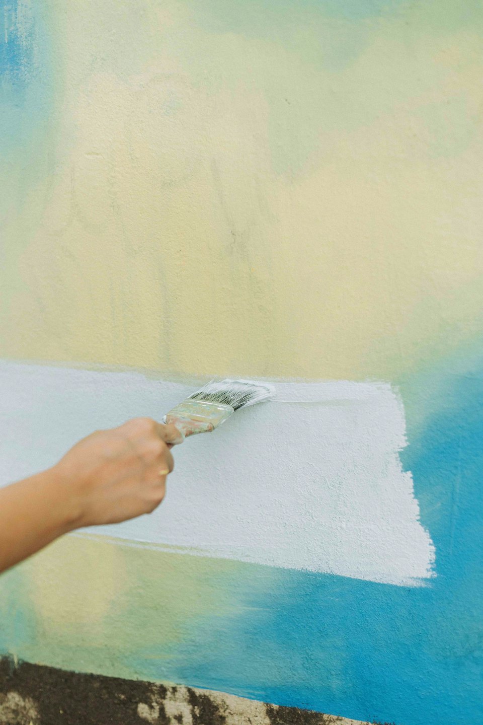 Una mano dipinge una striscia bianca su un muro testurizzato.
