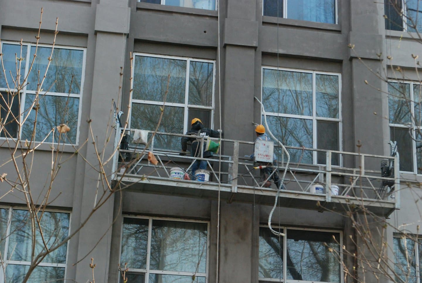 Operai edili applicano intonaco a un edificio da ponteggi sospesi.
